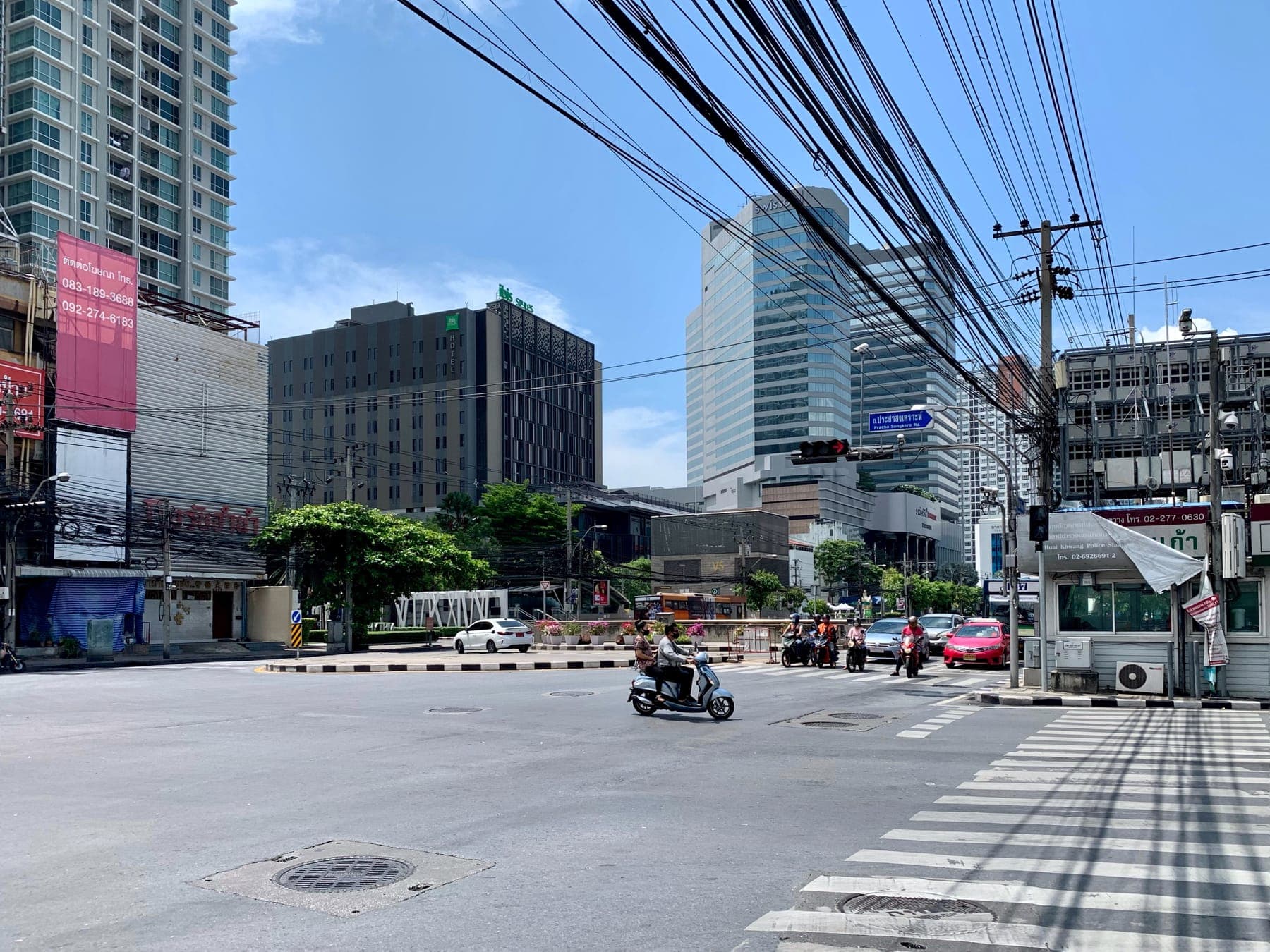 Street level in Huai Khwang at the Pracha Songkhro Road junction, the road sign and the Huai Khwang police box are both visible in frame, plus typical mid-rise condos and hotels